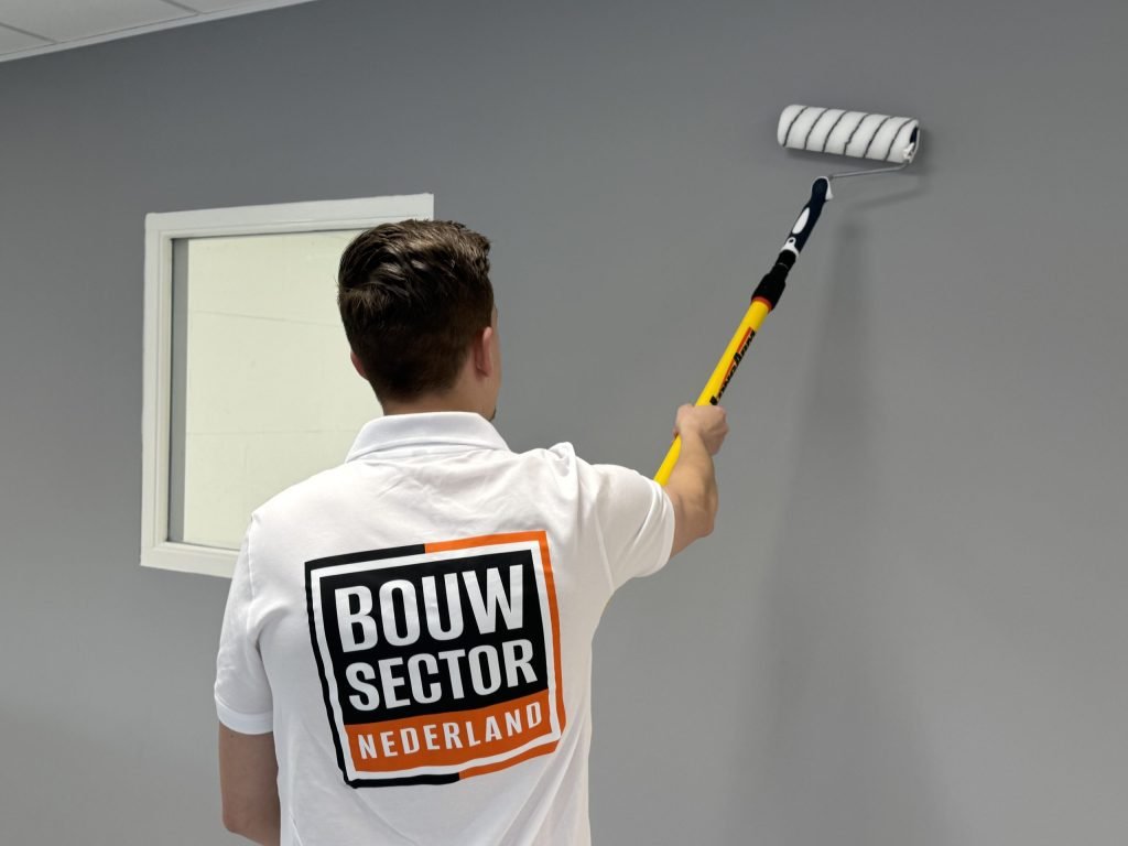 Schilder met het logo van Bouwsector Nederland op zijn rug zet een grijze muur naast een raam met de roller