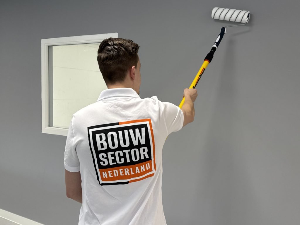 Schilder rolt de bovenrand van een grijze muur naast een wit binnenraam